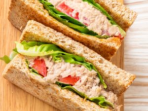 Tuna sandwich with lettuce and tomato slices on whole grain bread sliced diagonally