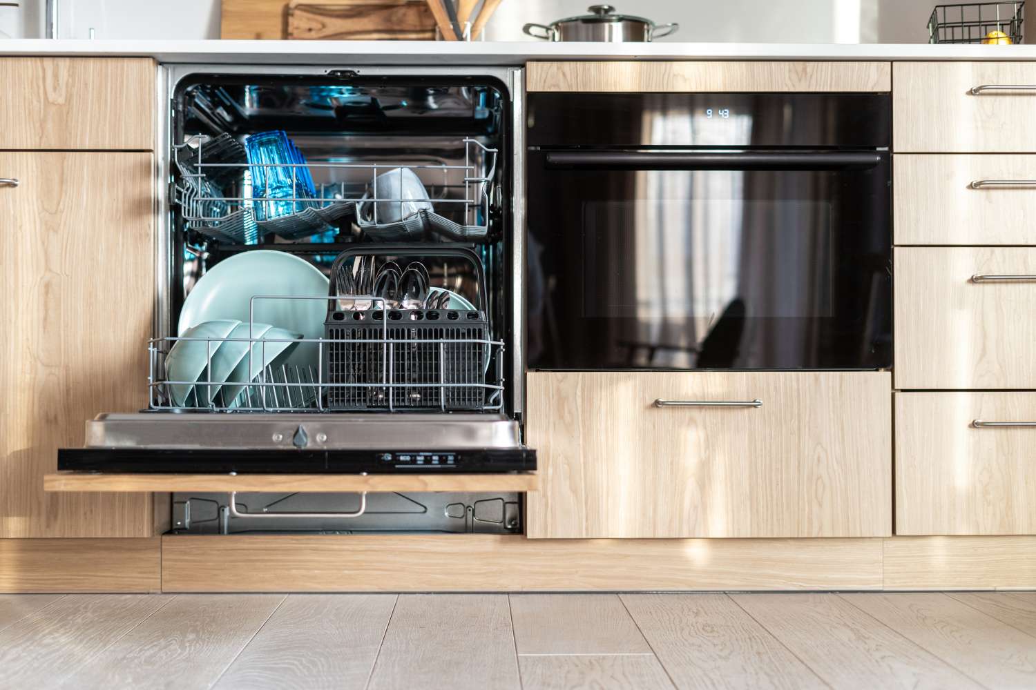 Open dishwasher in kitchen loaded with plates glasses and utensils
