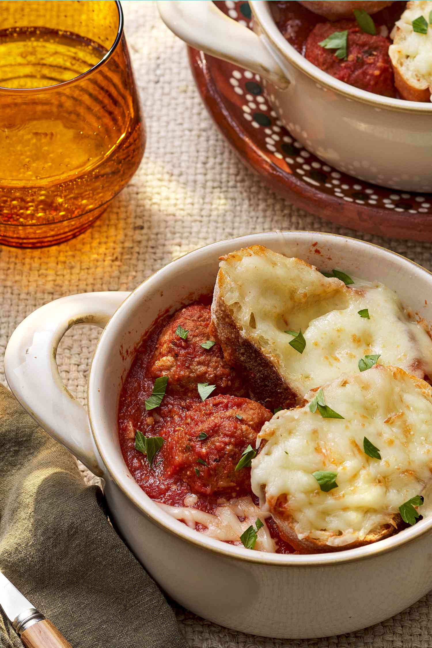 Bowl of meatball sub soup in a pot-like ramekin a rustic table setting with another ramekin of meatball sub and a glass of water