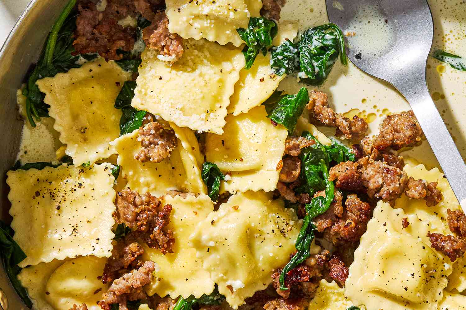 Closeup view of ravioli, Italian sausage and spinach topped with Parmesan cheese in a bowl with a spoon