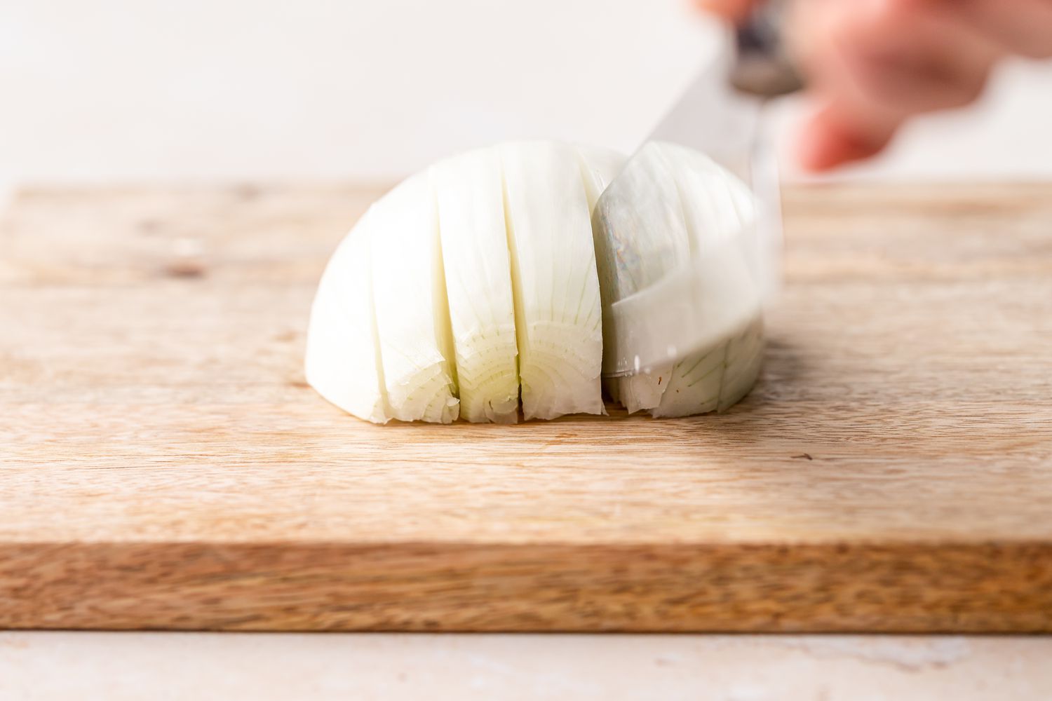Halved white onion on a cutting board being sliced in equal portions by a chef's knife