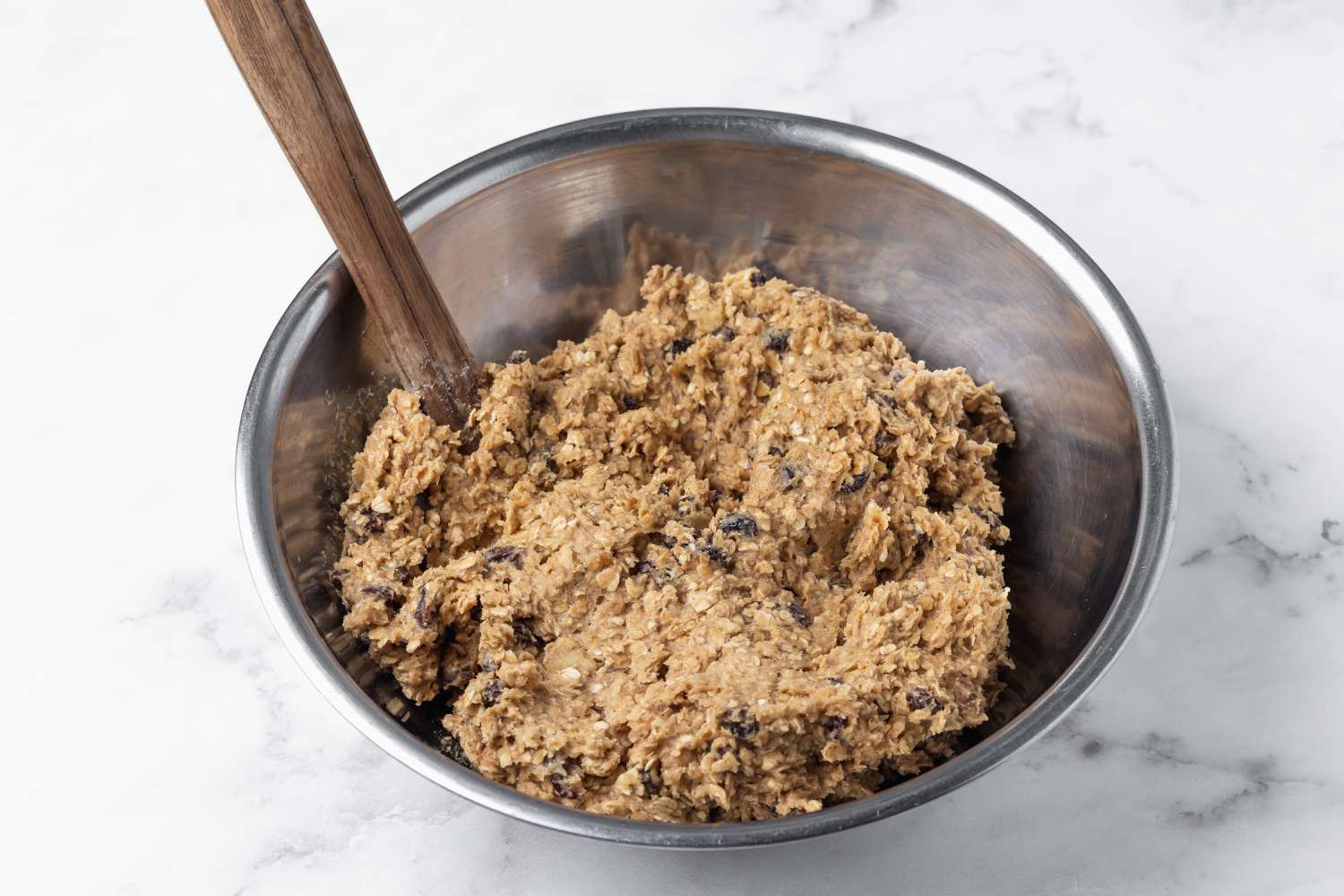 A metal bowl with the dough for Oatmeal Raisin Cookies inside.