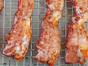 Four slices of oven baked bacon on a cooling rack.