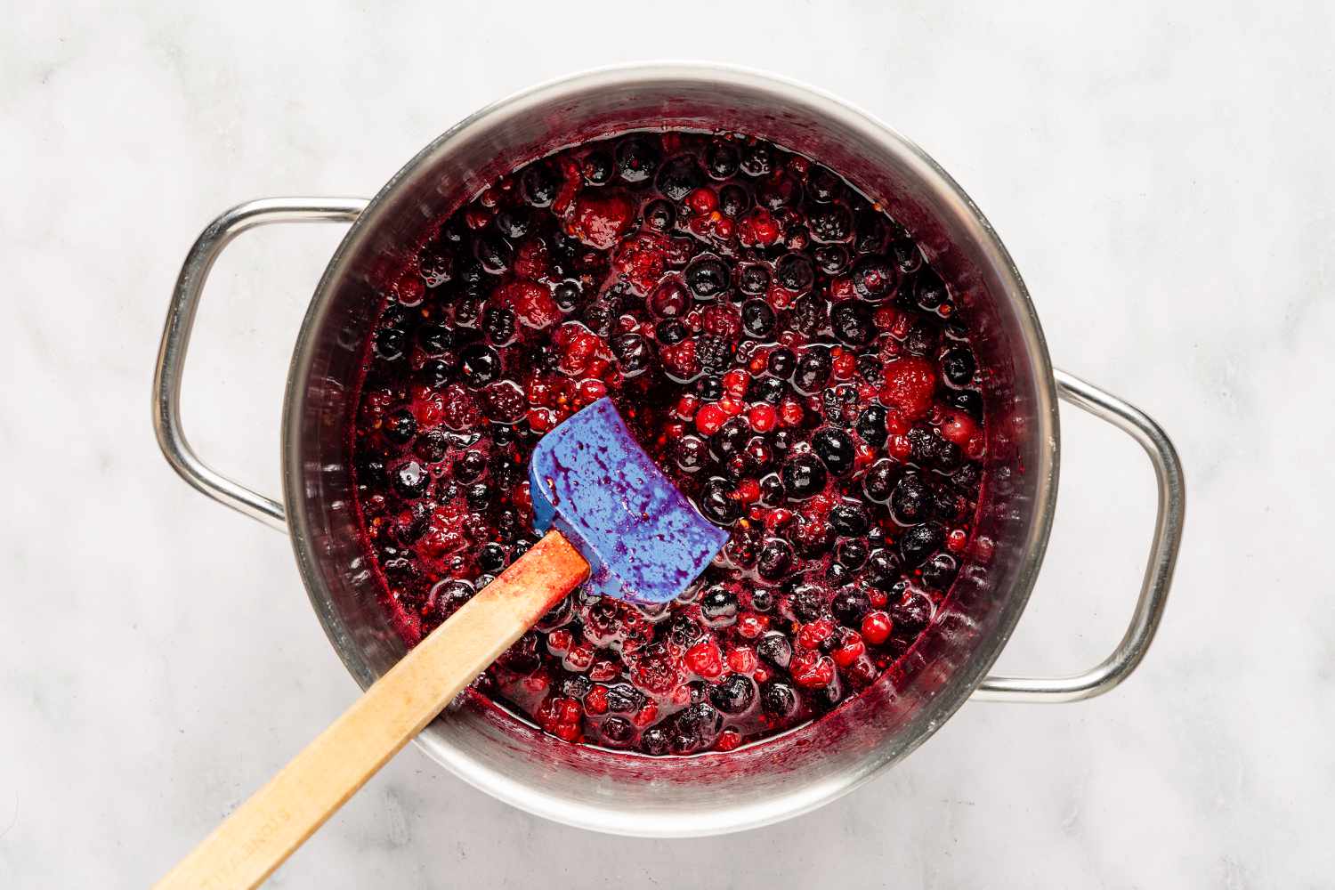 Overhead view of a metal pot and spatula with cooked frozen berries and sugar for Easy British Summer Pudding recipe