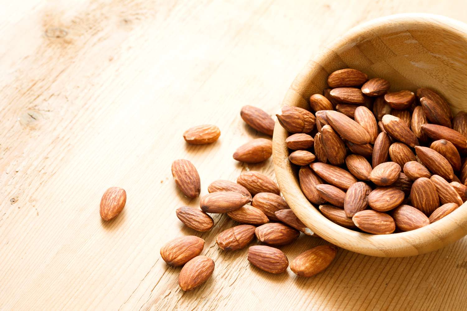 Almonds spilled from a wooden bowl on a table