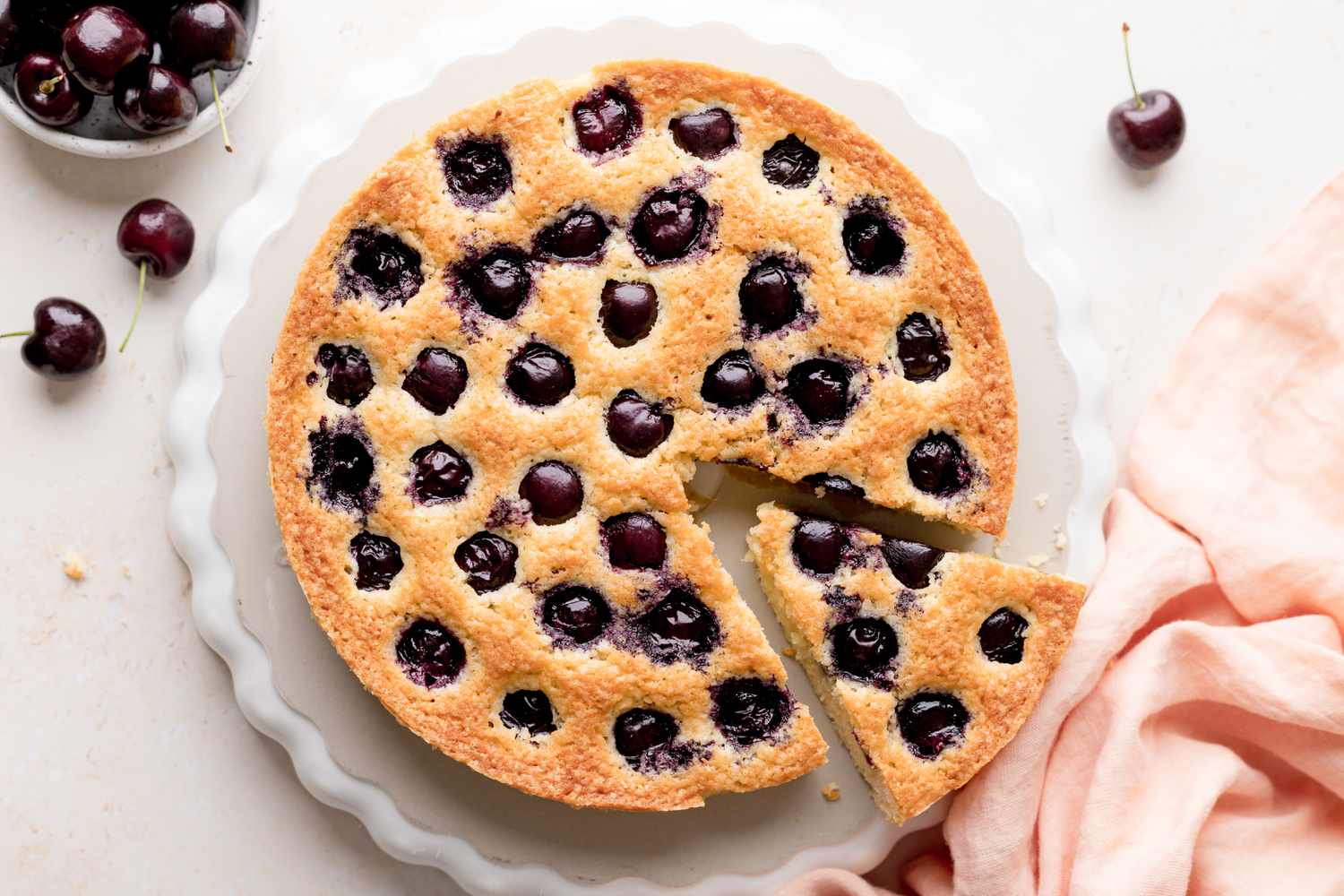Overhead view of a homemade cherry cake with a slice being removed.