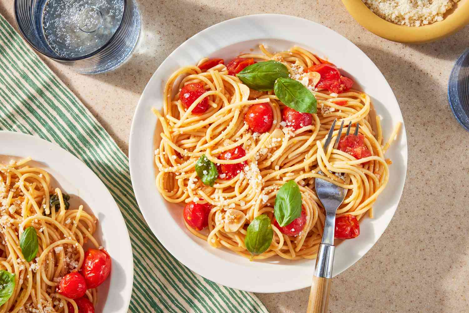 easy pasta pomodoro on two plates surrounded by glasses of carbonated water and a small bowl of parmesan