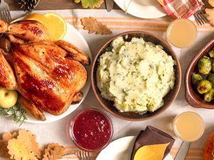 A Thanksgivingstyle meal with a roasted turkey mashed potatoes cranberry sauce and Brussels sprouts served on a decorated table