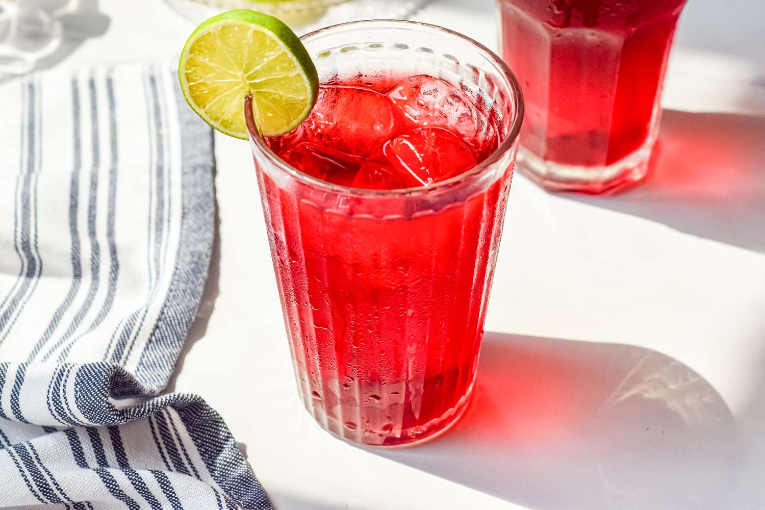 Agua de Jamaica (Hibiscus Tea) Served with Ice and a Lime Slice Next to a Kitchen Towel and Another Glass of Hibiscus Tea