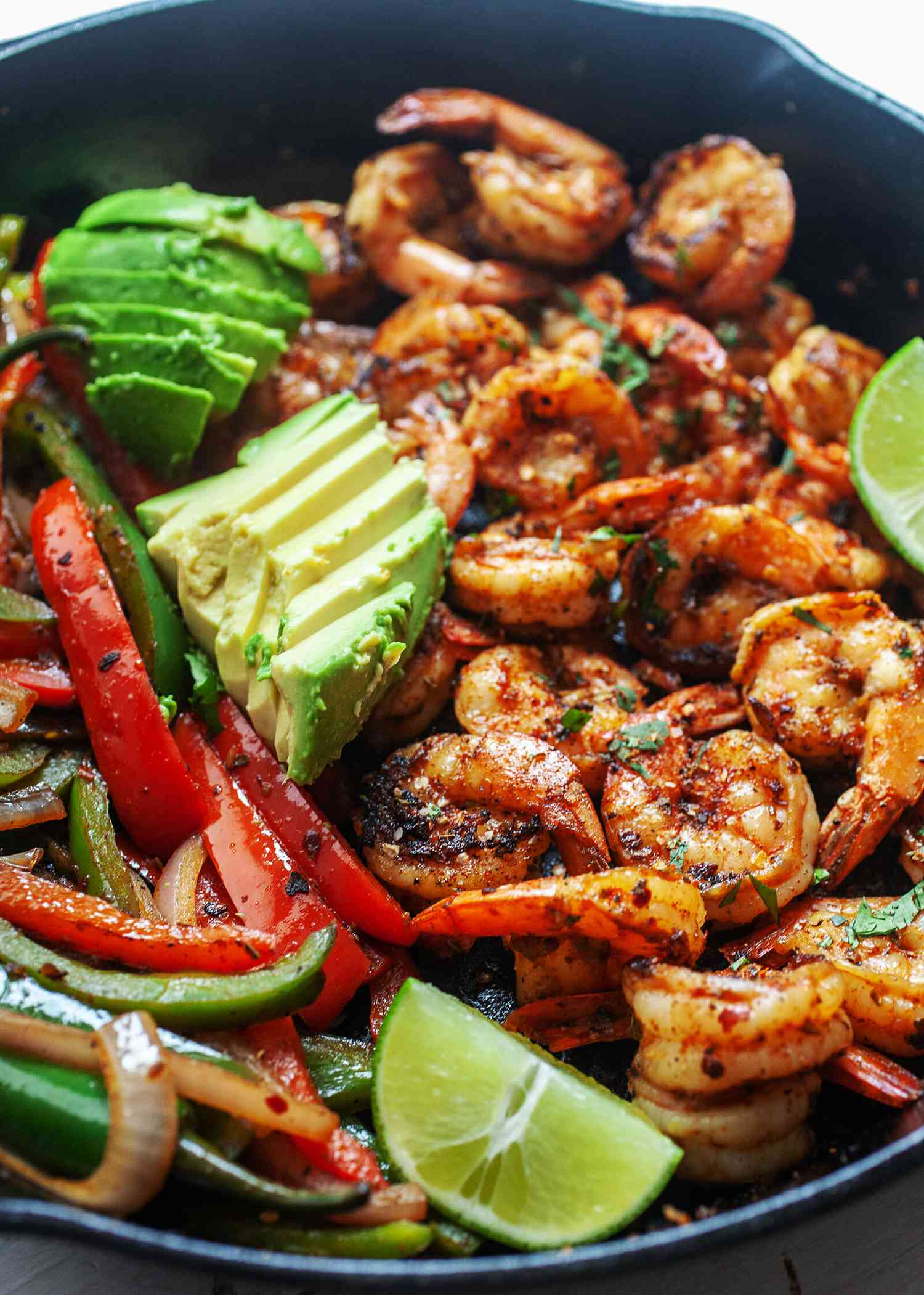 Shrimp fajitas in a pan topped with lime and avocado