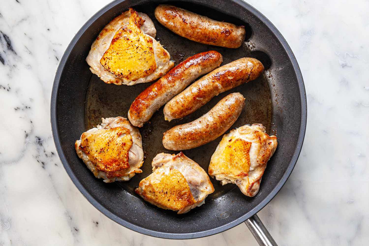 Chicken thighs and Italian sausages cooking in skillet.