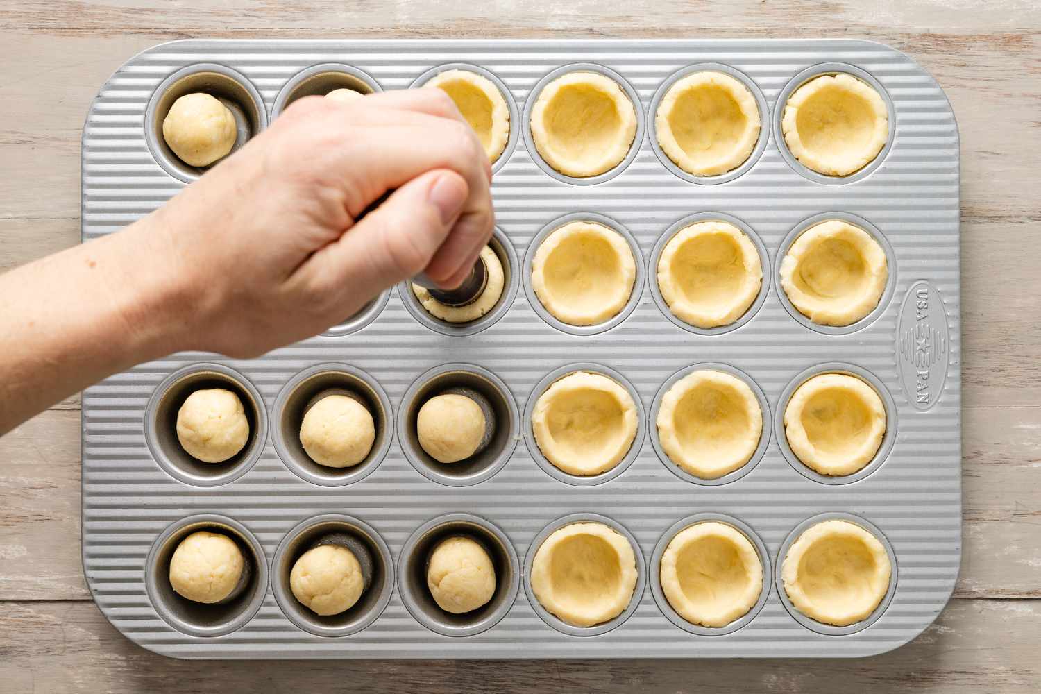 Tassie press flattening pecan pie cookie dough portions into the muffin pan 