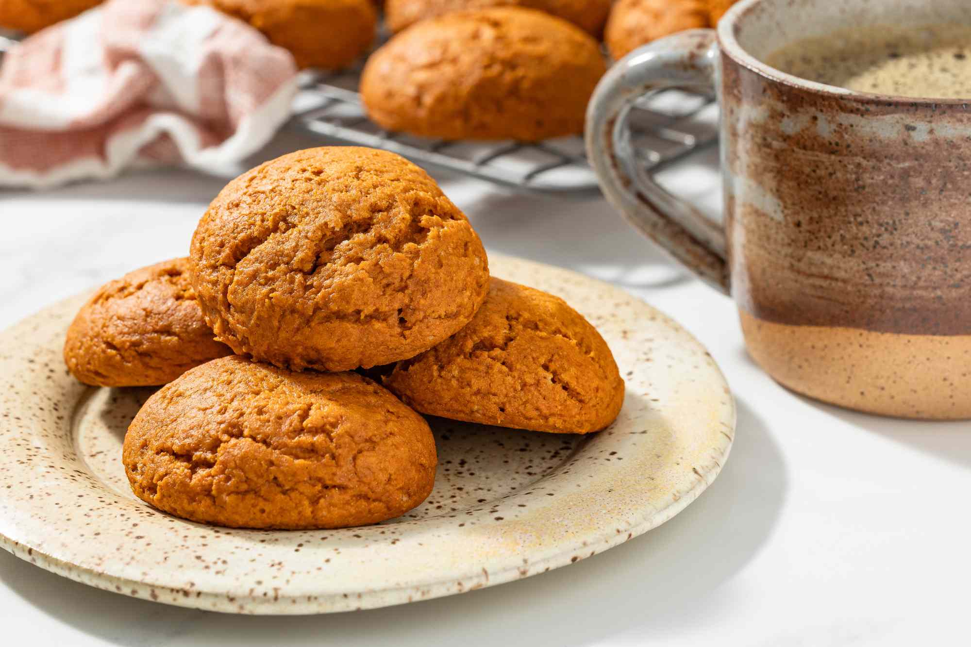 Plate of pumpkin quickies, and in the background, a cup of coffee and more quickies on a cooling rack next to a coral kitchen towel