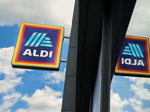 Aldi store signage reflecting on glass, against a background of clouds