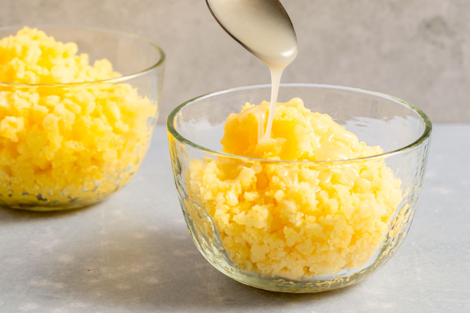 Two bowls of pineapple coconut granita, one being topped with cream from a spoon