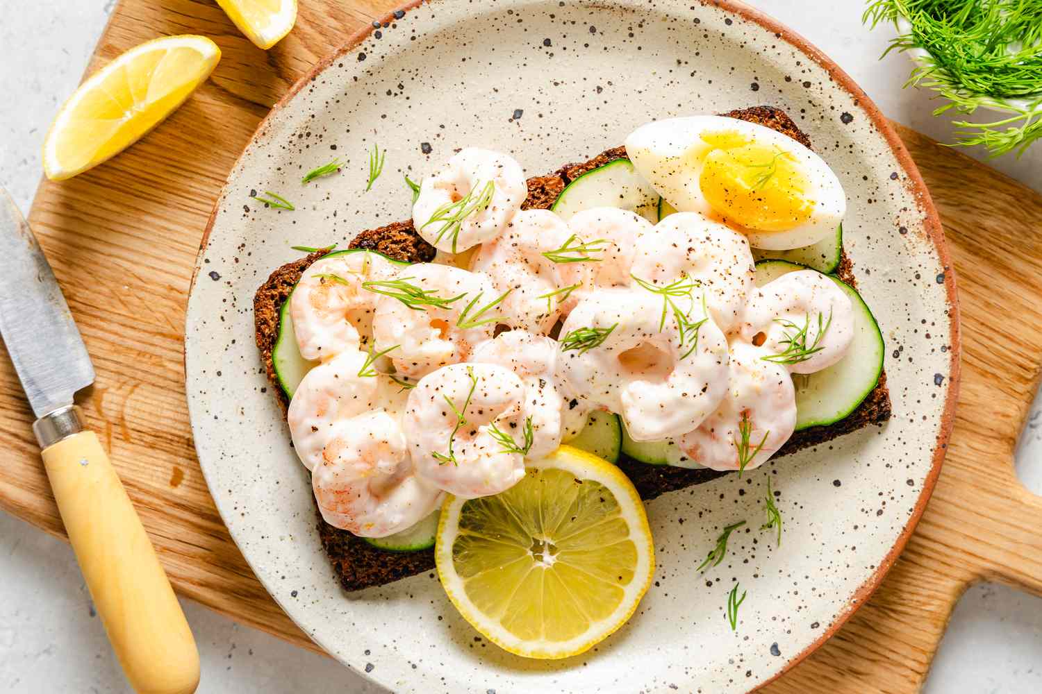 Scandinavian Shrimp Sandwich on a plate, garnished with wedge of a boiled egg, chopped fresh dill, and a lemon slice
