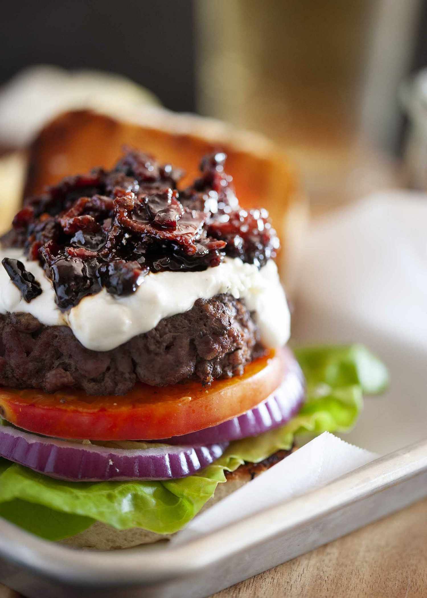 A burger with easy bacon jam on top of sauce, tomato, red onion and lettuce.