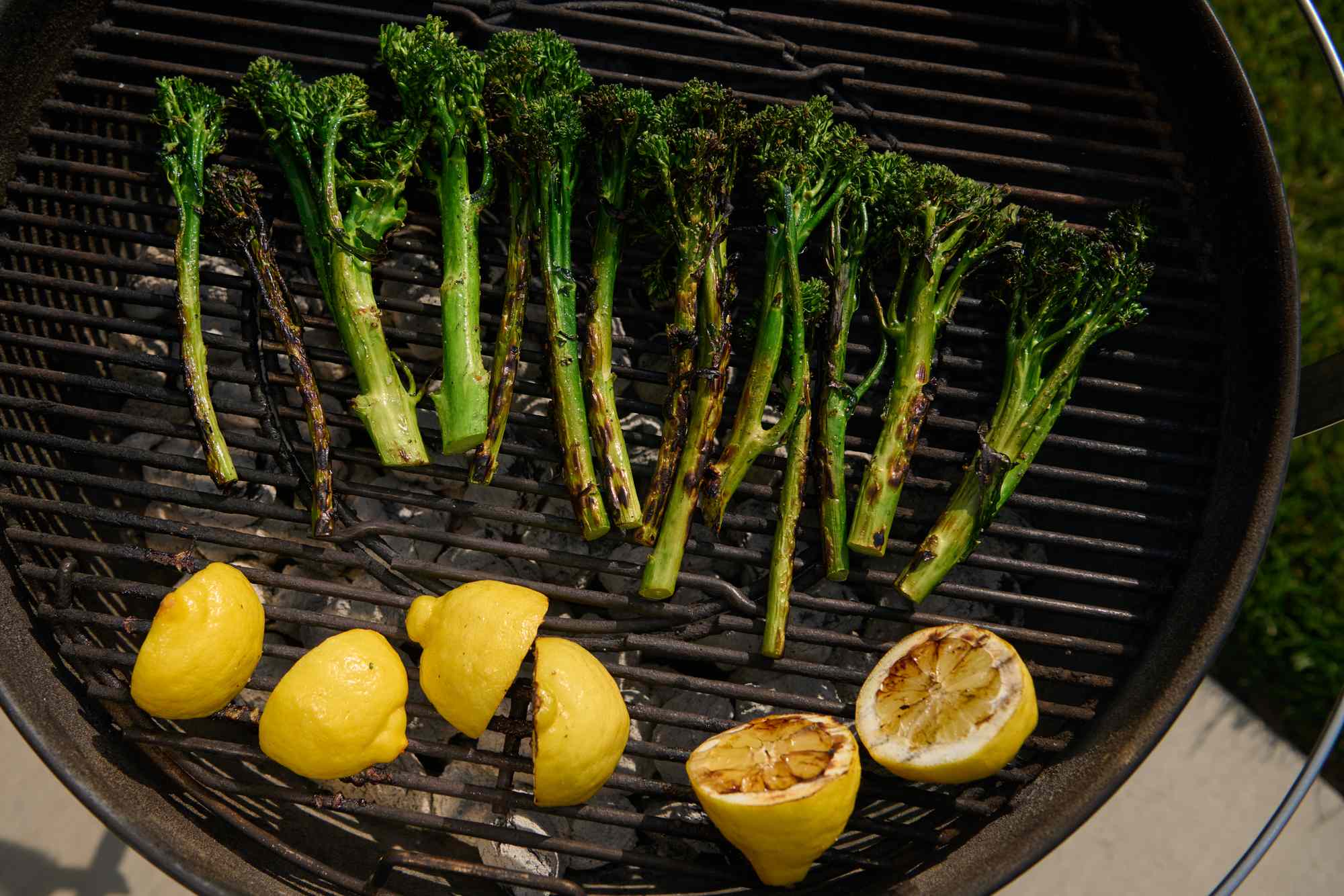 Grilled broccolini and lemon halves on a barbecue grill
