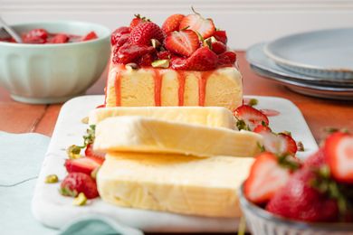 Strawberries and Cream Semifreddo Slices Cascading on a Platter Next the Rest of the Uncut Semifreddo on the Same Platter. Semifreddo Is Topped With Halved Fresh Strawberries and Strawberry Compote. In the Surroundings, a Bowl of Fresh Strawberries and a Stack of Plates.