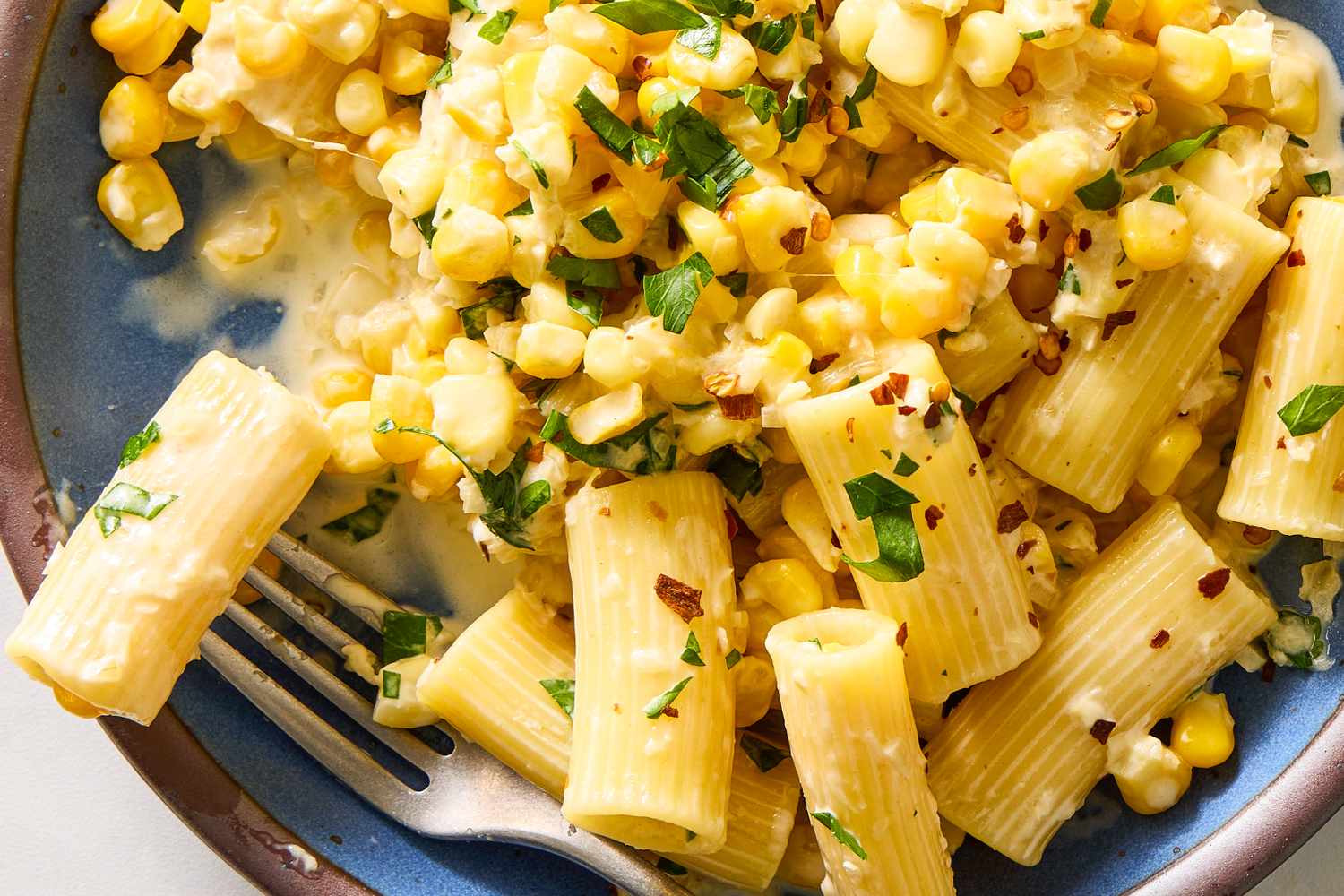 A dish of pasta garnished with corn and herbs served on a plate with a fork