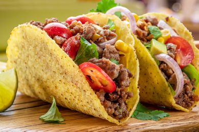 Two tacos on a wooden surface filled with ground beef sliced vegetables and garnishes