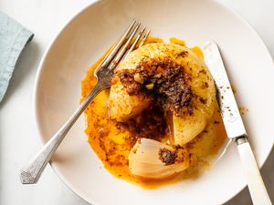 Whole cooked onion cut open served with sauce on a plate with a knife and fork