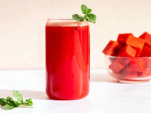 A glass of watermelon batido with mint next to a glass bowl of watermelon cubes