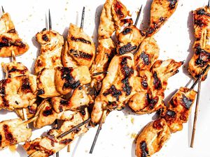 Chicken satay skewers grilled with charred marks, arranged on a white background