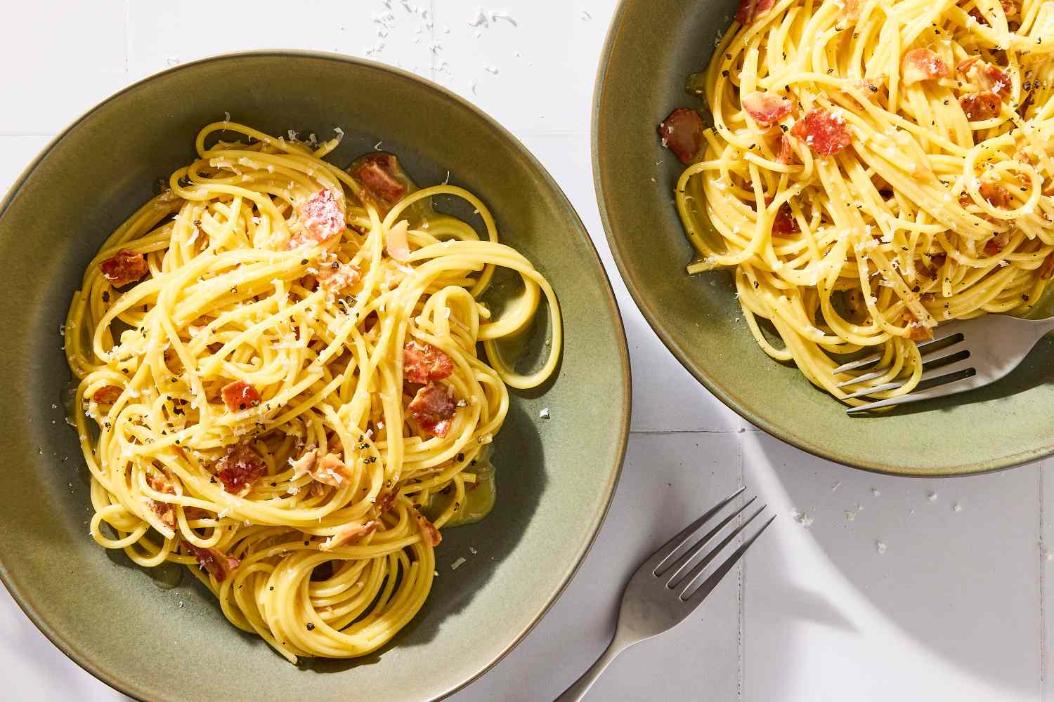 Two plates of pasta carbonara with forks placed next to them