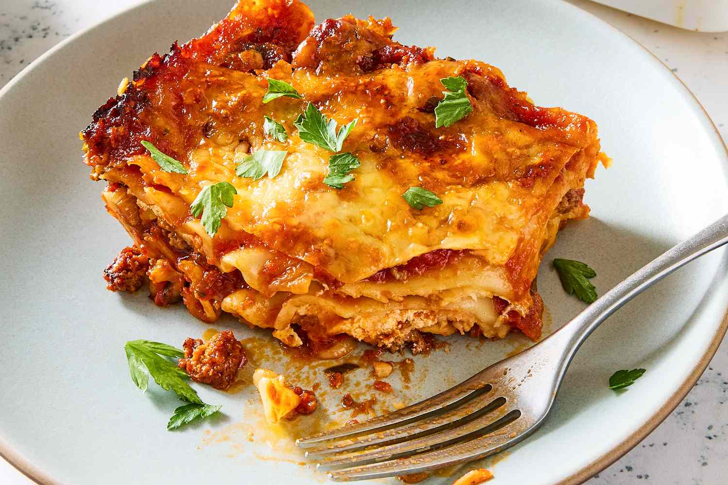 A slice of lasagna on a plate with a fork garnished with parsley