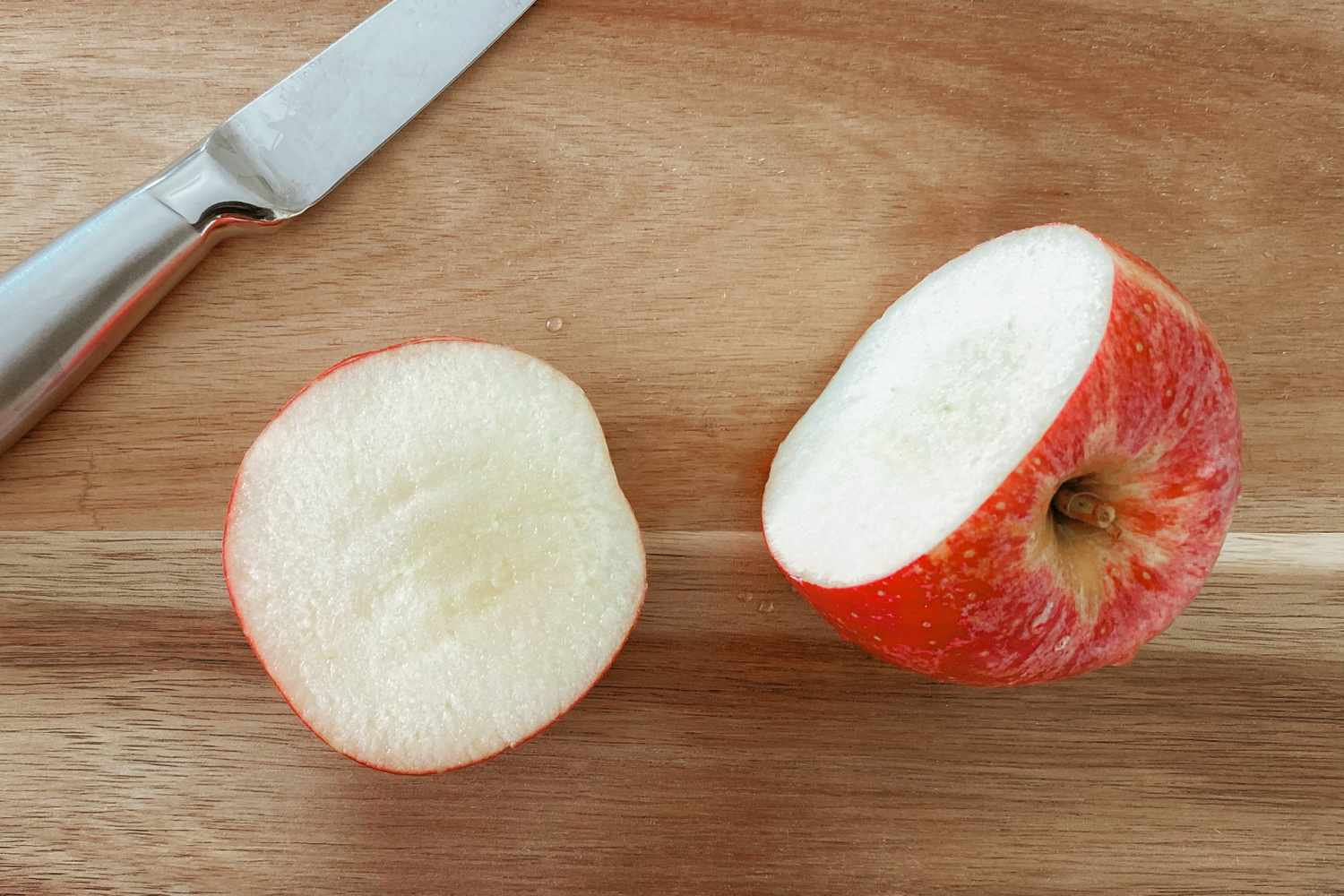 A knife and a halved apple on a wooden cutting board