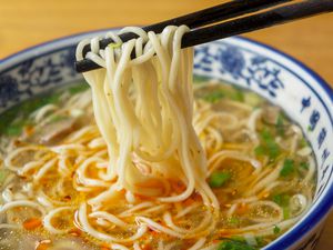Chopsticks lifting ramen noodles from a bowl of soup with garnish