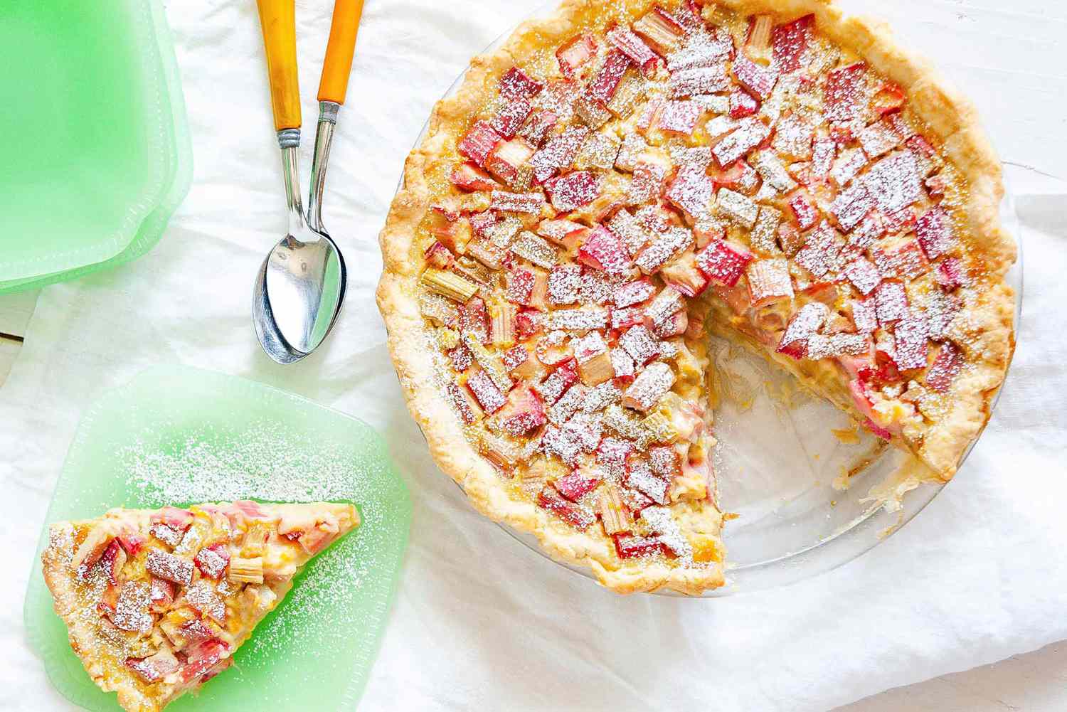 A rhubarb custard pie with a slice taken out of it, set aside on a green plate
