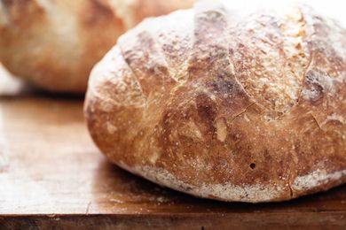 Side view of no-knead dutch oven bread on a cutting board. The crust is deep golden brown and a second loaf is behind the first.