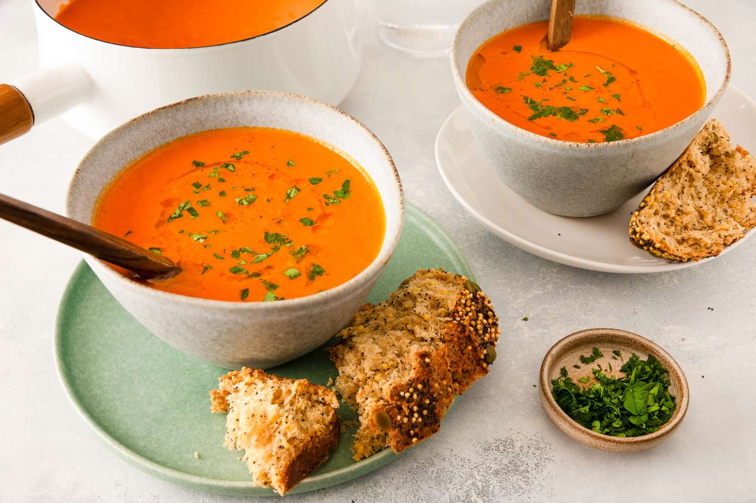 Bowls of pumpkin tomato soup with garnished bread served on a table
