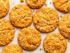 anzac biscuits laid out on a white surface, with some cookie crumbs surrounding them