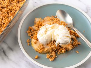 Overhead view of a teal plate of 5-ingredient vanilla pear crisp recipe topped with vanilla ice cream and next to a spoon and the baking dish from the crisp