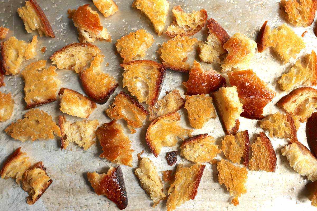 Rustic homemade croutons scattered on a baking sheet to be used in a bitter green and citrus salad.