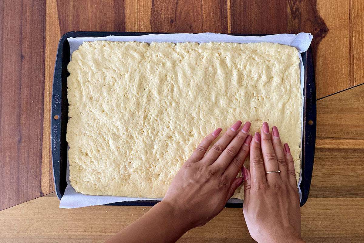 Dough being pressed into a parchment lined baking sheet to make the best gluten free cinnamon rolls.