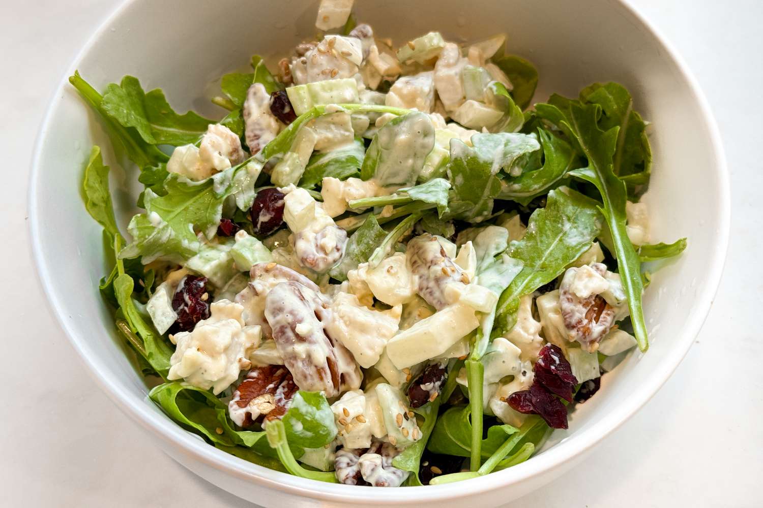 Chicken salad with cranberries and pecans served on top of arugula in a bowl