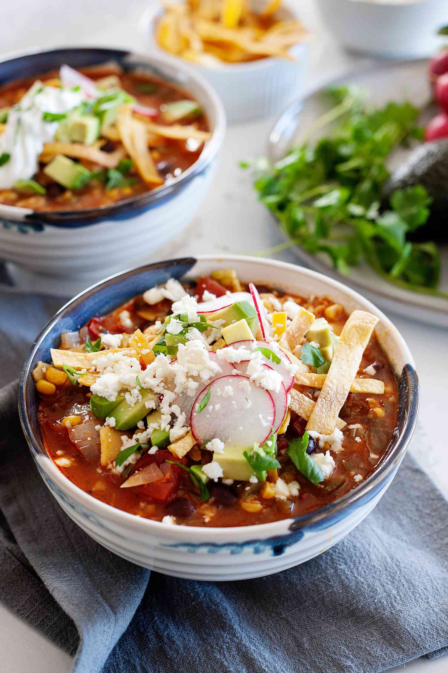 Meatless tortilla soup in a bowl topped with shredded cheese, sour cream, and tortilla strips.