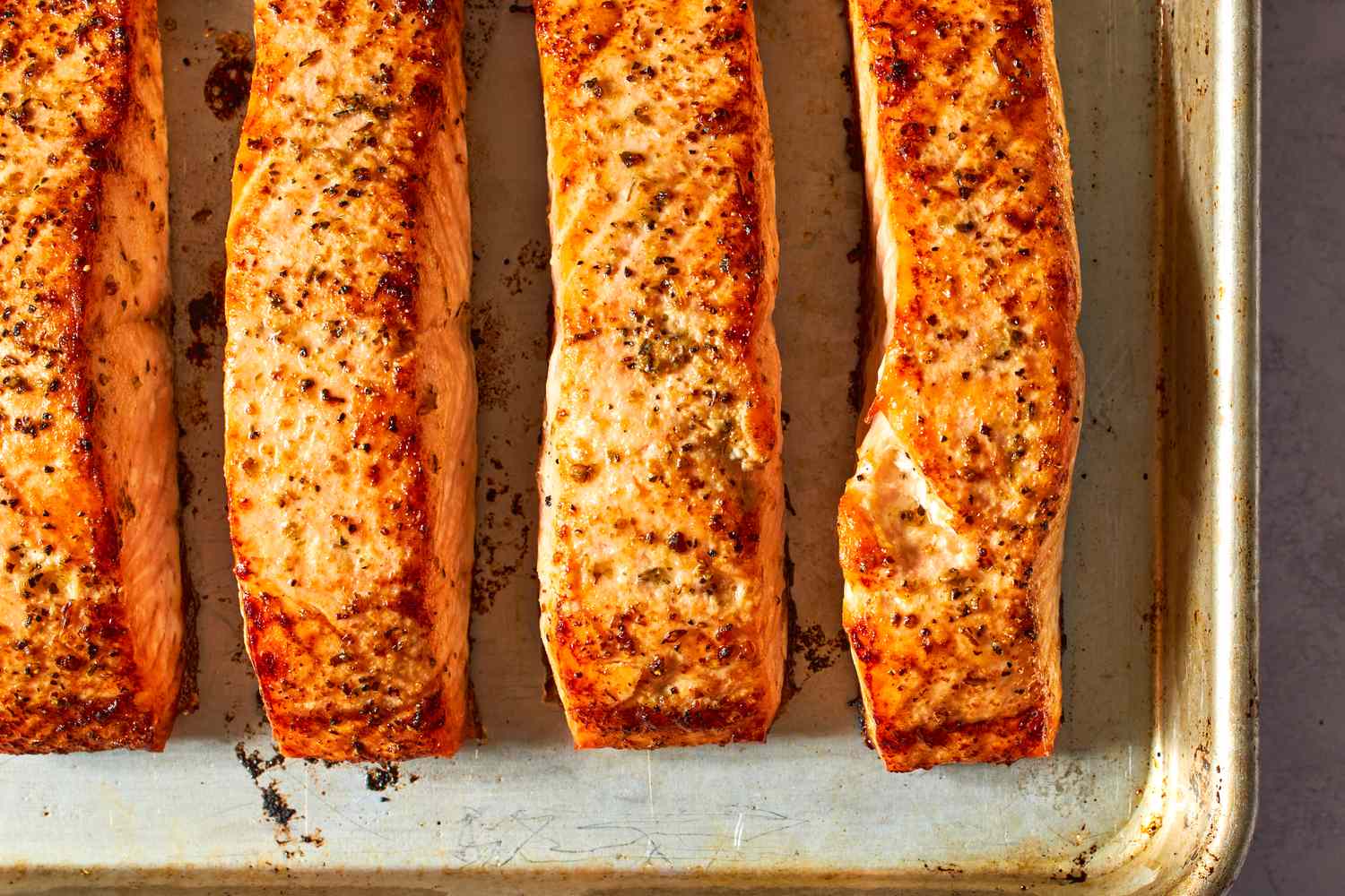 Four salmon fillets baked on a tray, garnished with seasoning