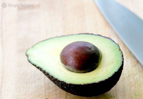 An avocado half with the seed intact placed on a wooden surface next to a knife