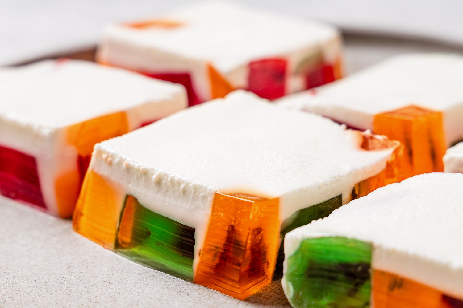 Closeup of squares of colorful jello pieces topped with a cream layer