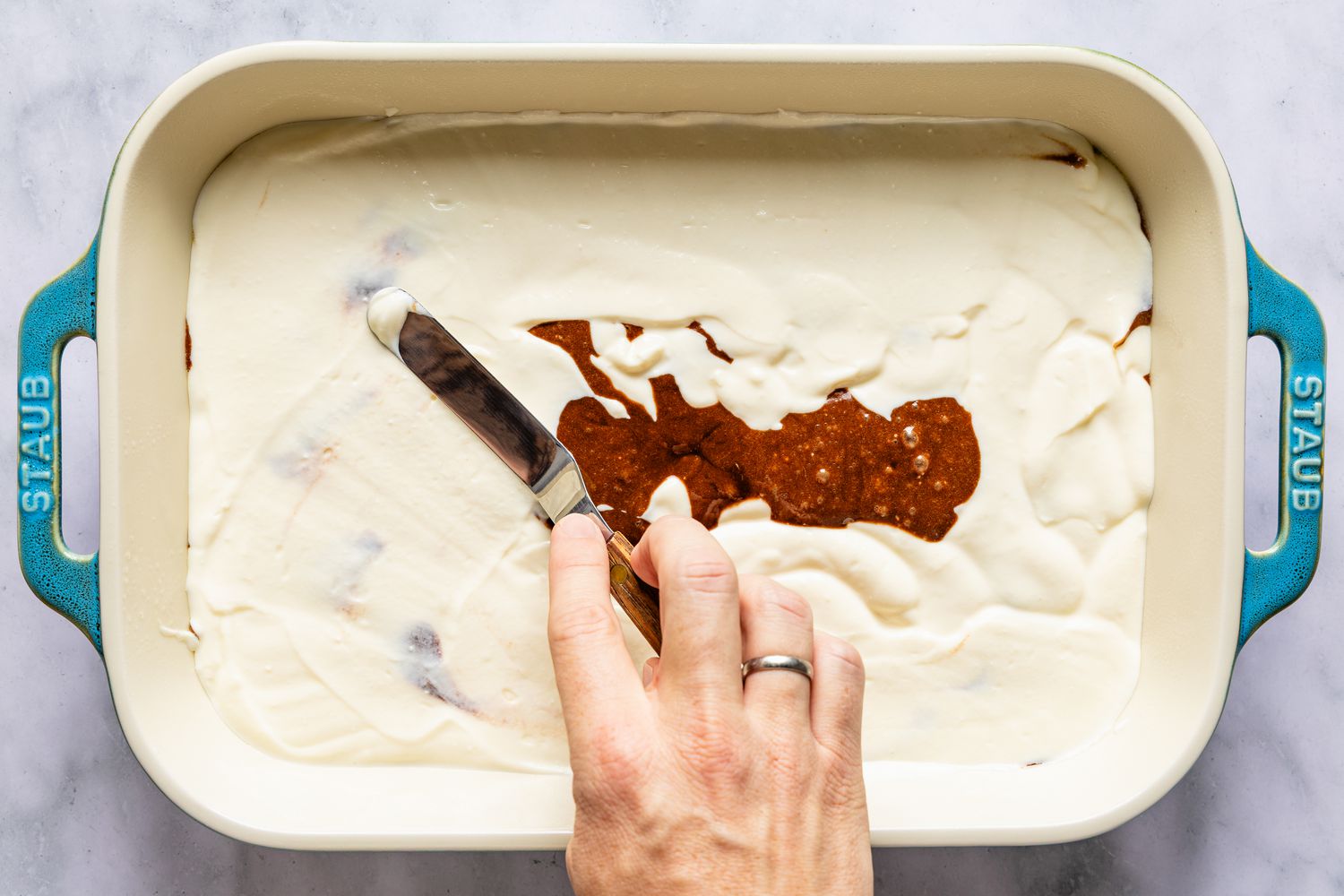 Hand spreading ricotta cream layer over cake batter layer for Italian love cake recipe, in a Staub baking dish