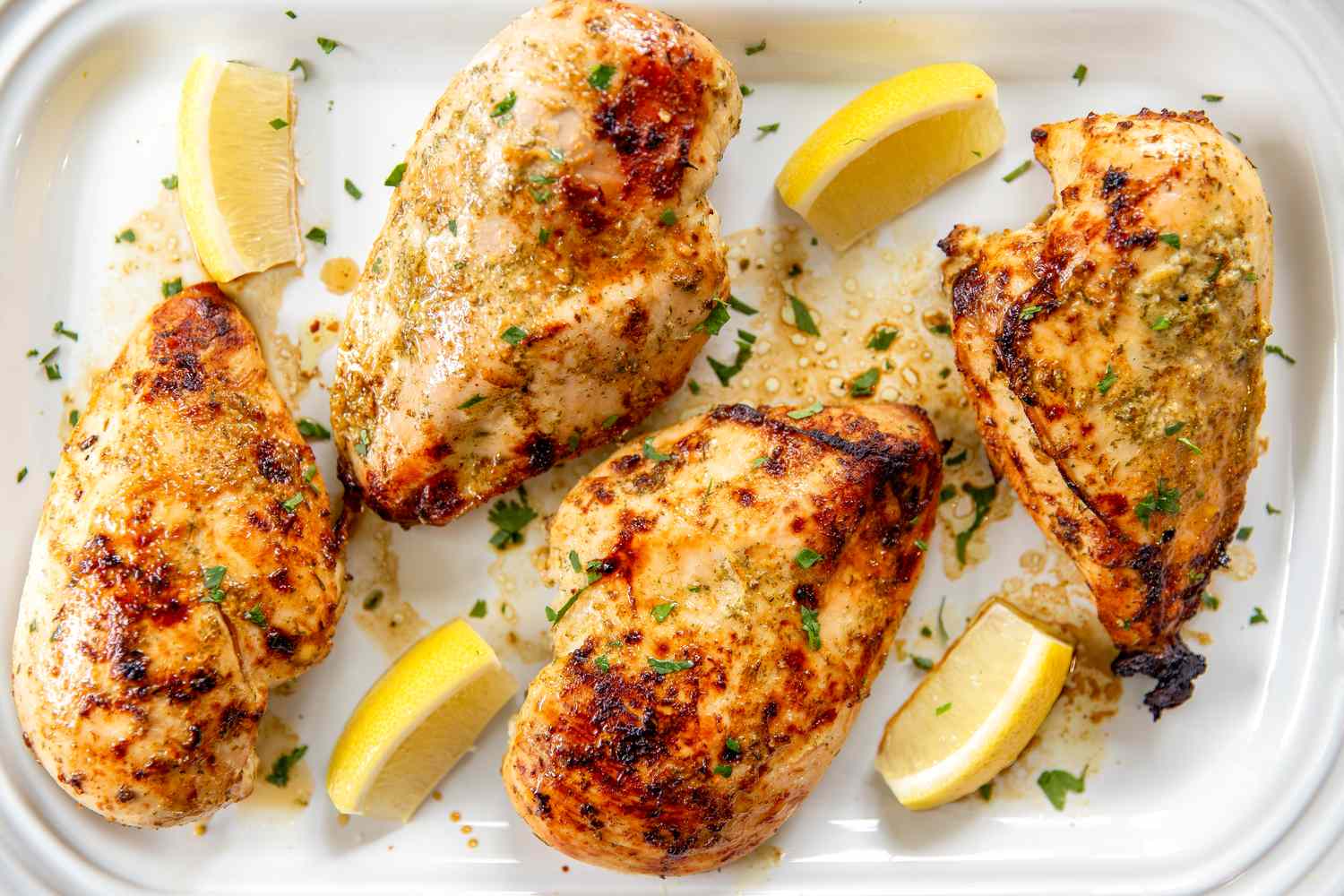 Cooked chicken breasts garnished with herbs alongside lemon wedges