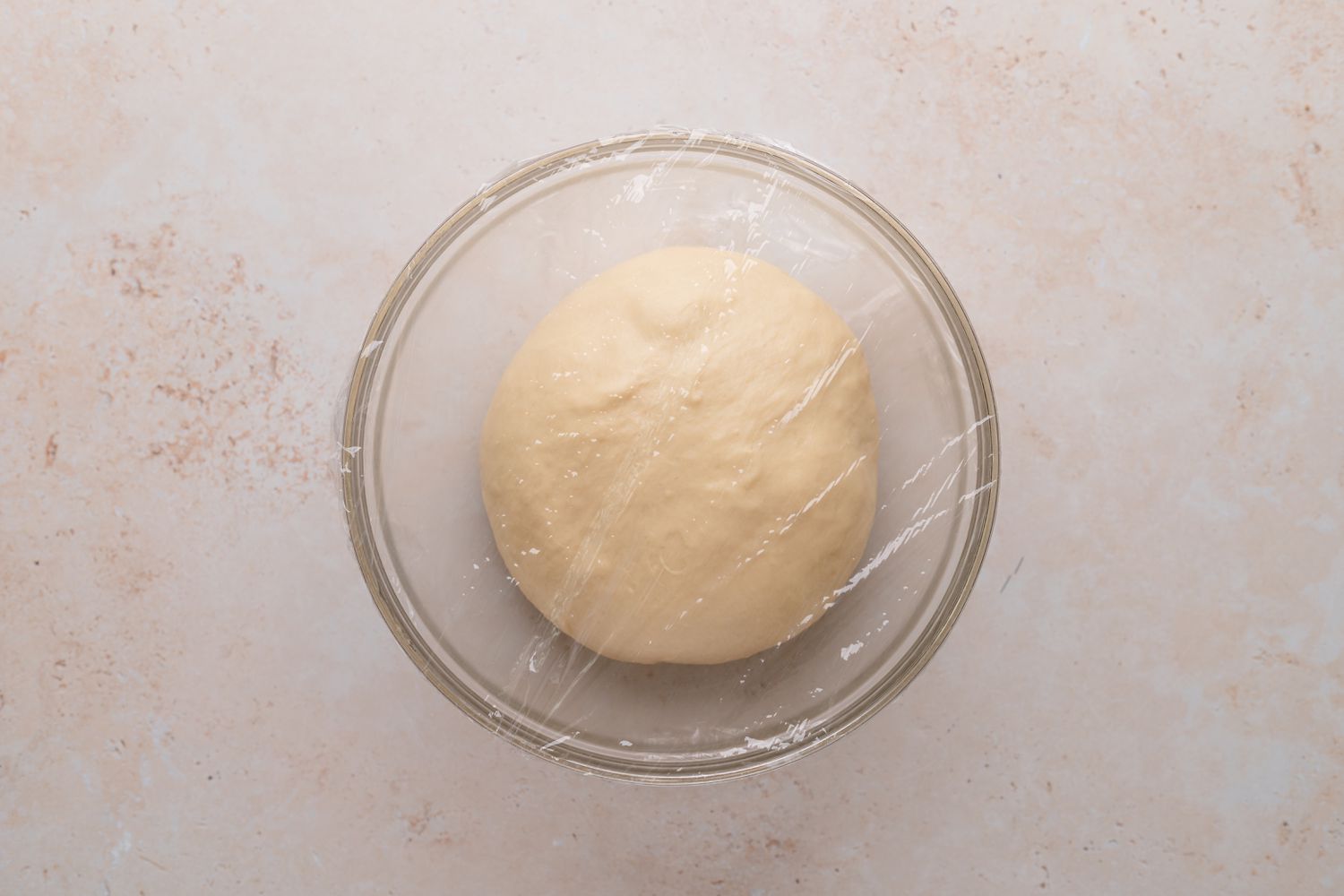 Braided chocolate babka dough rising in a glass bowl.