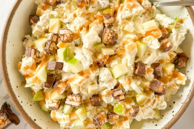 A bowl of Snickers salad with chopped apples, Snickers pieces, and caramel drizzle, served in a ceramic dish