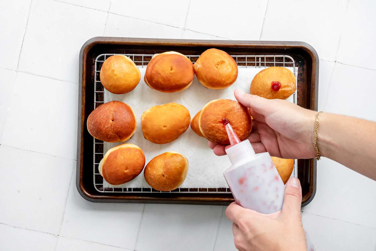 Sufganiyot (Israeli Jelly Donuts) Filled with Jam with the Squeeze Bottle after Poking a Hole in the Middle of the Donut