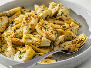 Side view closeup of a large serving plate with garlic & herb sautéed artichokes, with a spoon on the plate